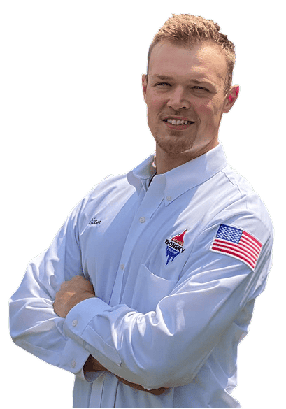 Man in a light blue button-up shirt with an American flag patch and a Dorsey logo, standing with arms crossed and smiling at the camera.