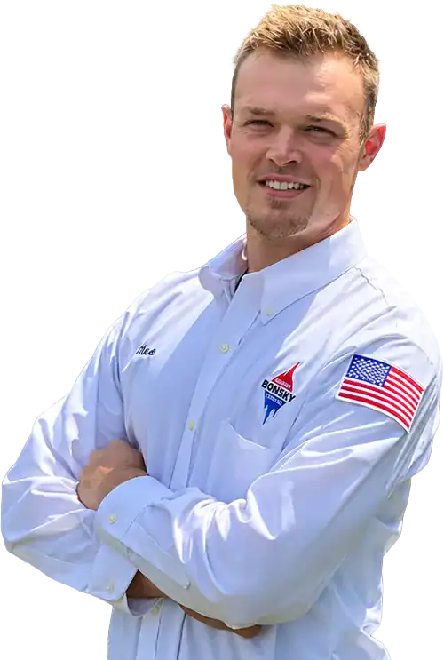Man wearing a white button-down shirt with an American flag patch and a company logo, standing with arms crossed and smiling at the camera.